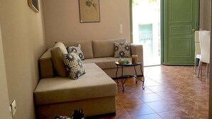 Un soggiorno con un divano color beige, cuscini decorati, un tavolino piccolo con bevande e una porta verde.