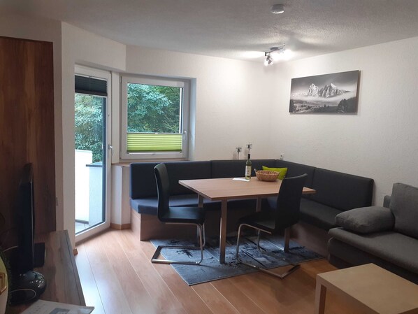 A compact living space with a dining table, two sofas, a TV, and a window with blinds.