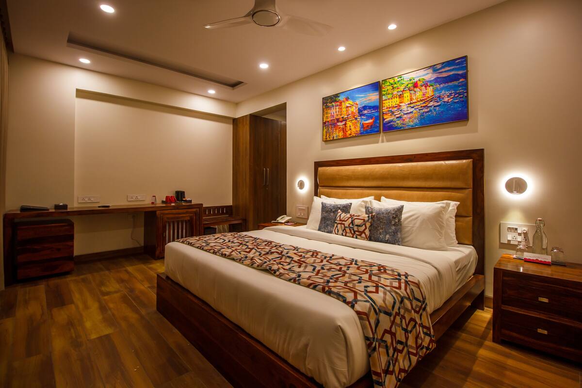 Ein modernes Schlafzimmer mit einem großen Bett, einem Schreibtisch und einem Sessel. An der Wand hängt ein Gemälde, und eine Deckenventilator ist angebracht.