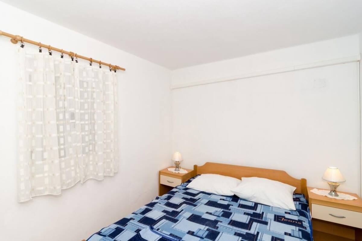A bedroom with a bed, two bedside tables with lamps, a curtain, and a wall-mounted light switch.