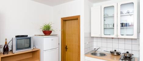 A compact kitchen with white cabinets, a built-in microwave, a small refrigerator, a wooden door, and a sink with a stove.