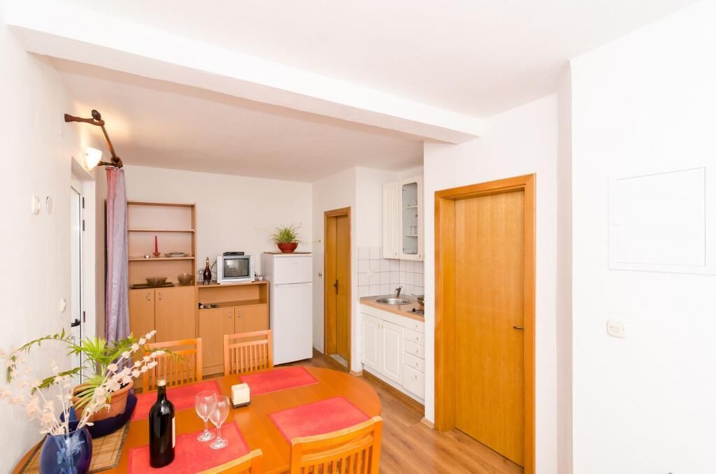 Cocina compacta con alacenas blancas, puerta de madera y zona de comedor con mesa y sillas.