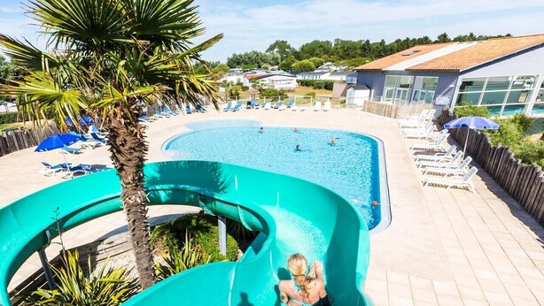 Ein Swimmingpool mit Wasserrutsche, Liegestühlen und Palmen.
