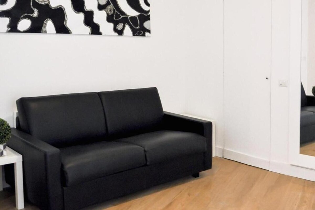Een zwarte bank in een kamer met houten vloeren en een witte muur.