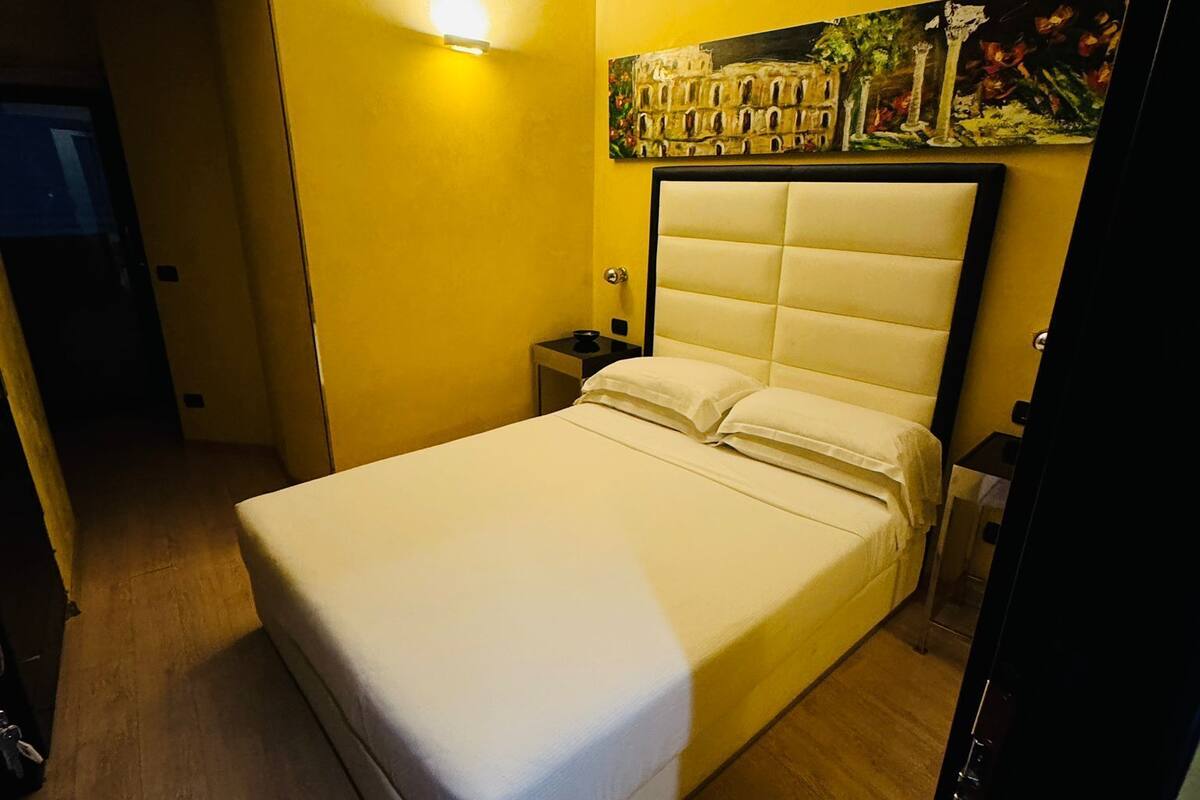 A bedroom with a bed, a nightstand, a wall-mounted light, and a painting.