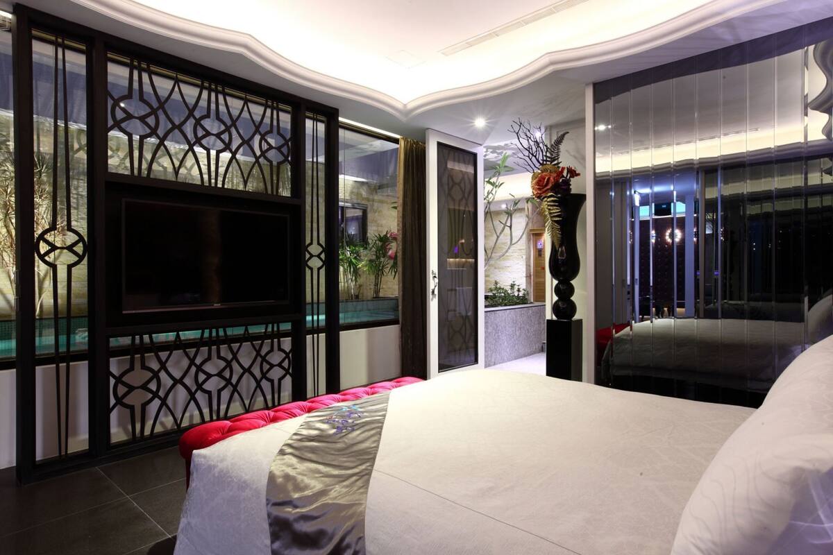 Une chambre d’hôtel moderne, dotée d’un grand lit, d’une télévision, d’une plante décorative et offrant une vue sur l’extérieur.