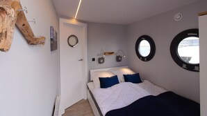 Een slaapkamer met een bed, twee wandlampen, een ronde spiegel en een raam met uitzicht.