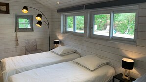 A bedroom with two beds, a chair, and a window with a view of greenery. - Villa Marguerite à Arès, Près du Bassin D'arcachon et de L'ocean (Arès)