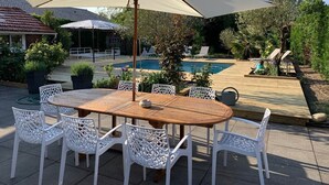 A wooden table with white chairs and a large umbrella in a garden setting. - Villa Marguerite à Arès, Près du Bassin D'arcachon et de L'ocean (Arès)