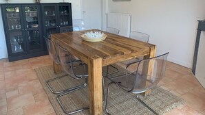 A dining area with a wooden table and clear chairs, a black cabinet with glass doors, and a painting on the wall. - Villa Marguerite à Arès, Près du Bassin D'arcachon et de L'ocean (Arès)