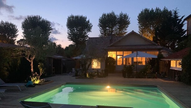 A rectangular swimming pool with a wooden deck, surrounded by lounge chairs and a house in the background. - Villa Marguerite à Arès, Près du Bassin D'arcachon et de L'ocean (Arès)