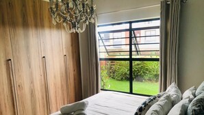 A bedroom with a large window, wooden wardrobe, and a chandelier. - The blyde 3 bedroom crystal Lagoon beach  (Pretoria)