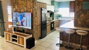 A modern kitchen with a stone accent wall, a TV, and a bar area with stools. - The blyde 3 bedroom crystal Lagoon beach  (Pretoria)