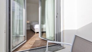 Un estrecho pasillo que conduce a un dormitorio con cama, mesita de noche y ventana con cortinas.
