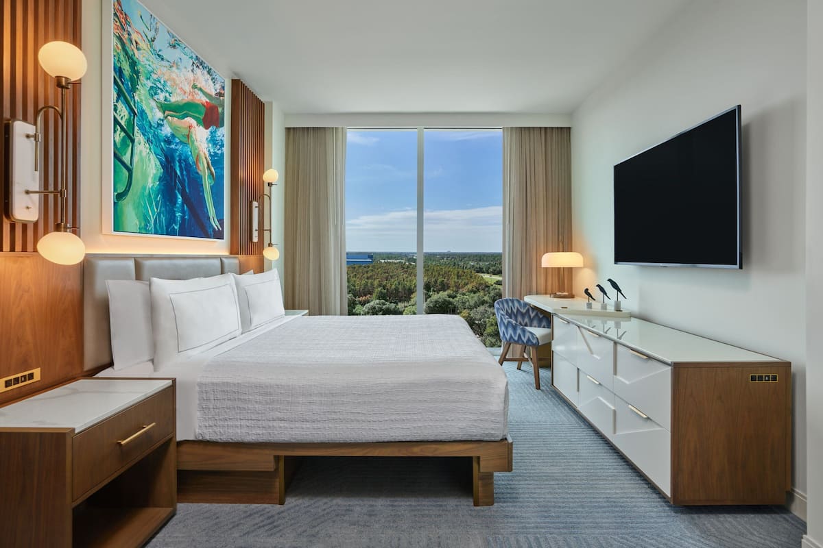 Een moderne hotelkamer met een groot bed, een flatscreen televisie, een bureau met stoel, en een groot raam met een mooi uitzicht.