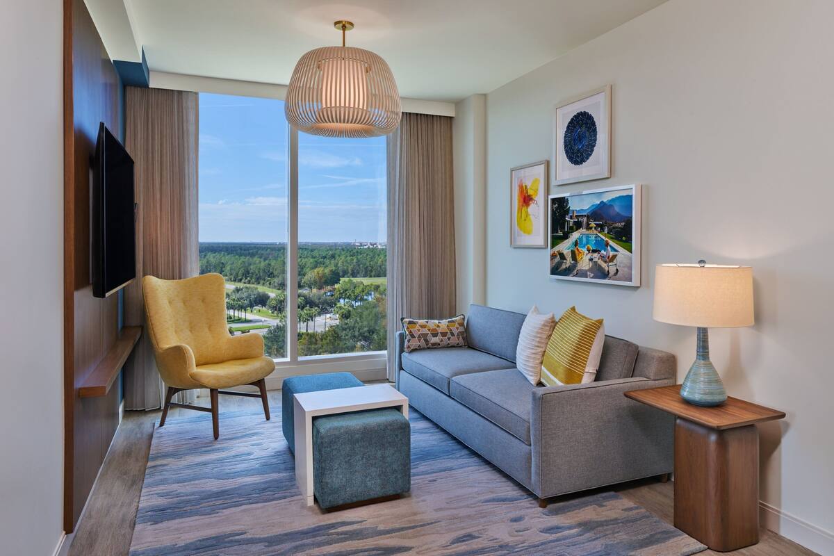 Een moderne hotelkamer met een groot raam, een bank, een stoel, een televisie en kunstwerken aan de muren.