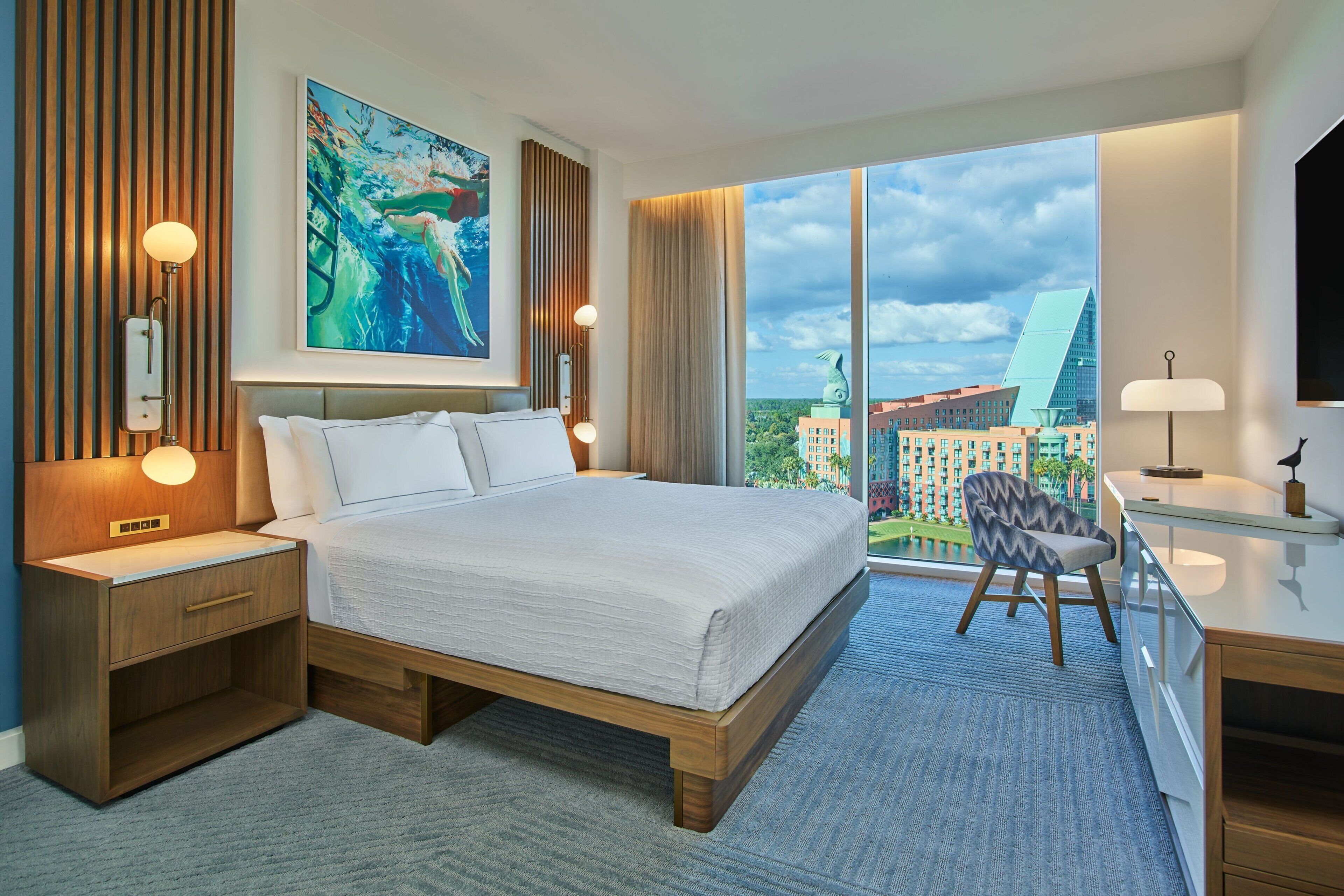 A modern hotel room with a large bed, a desk, and a view of the cityscape.