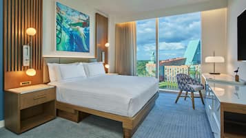 A modern hotel room with a large bed, a desk, and a view of the cityscape.