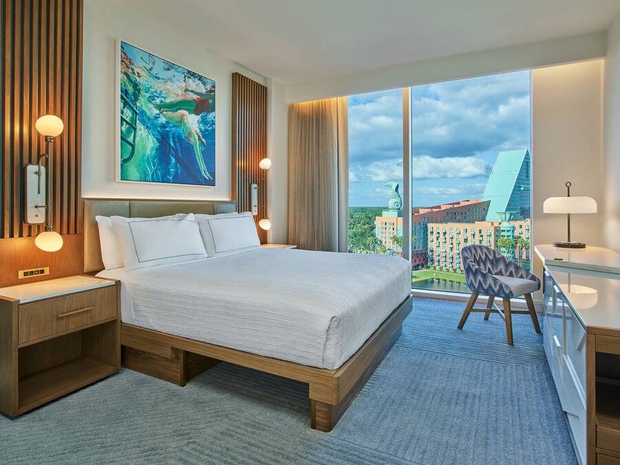 A modern hotel room with a large bed, a desk, and a view of the cityscape.