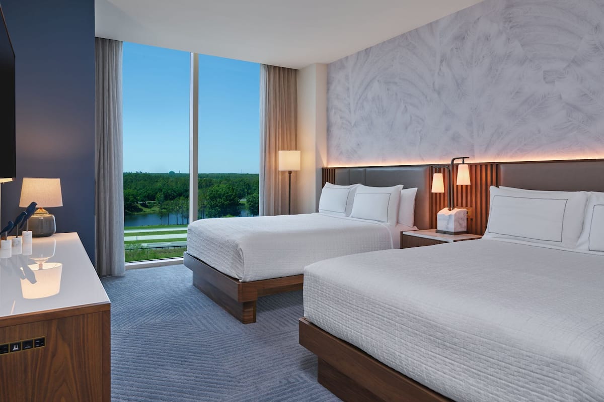 Een hotelkamer met twee bedden, een bureau en uitzicht op een meer.