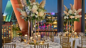 Un restaurant où les tables sont dressées pour le dîner, avec des arrangements floraux et des bougies en guise de décoration.