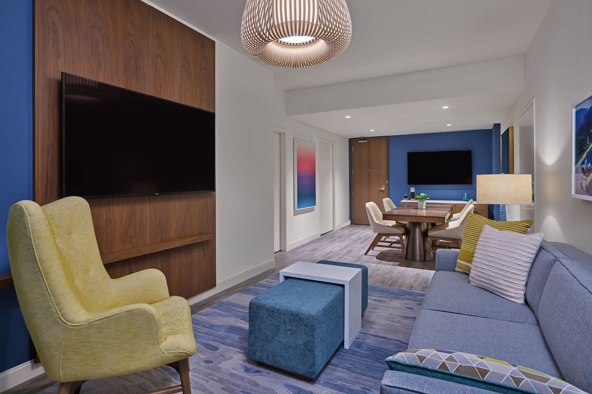 Een moderne hotelkamer met een flatscreen televisie, een bank, een stoel, een eettafel en een lamp.