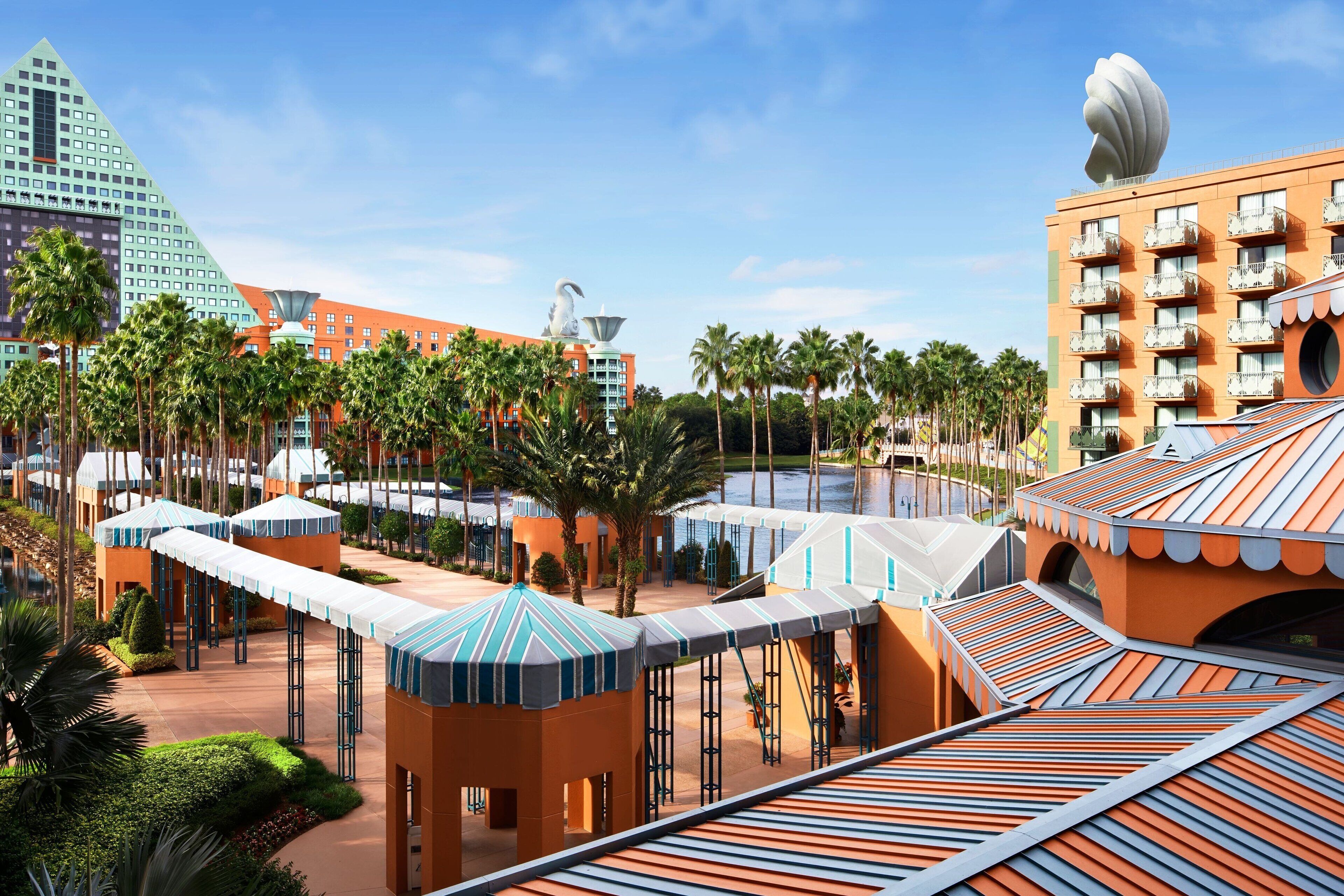 A resort with a modern architectural design, featuring a large building with a unique spherical structure on top, a series of smaller buildings with striped roofs, and a well-maintained palm tree-lined courtyard.