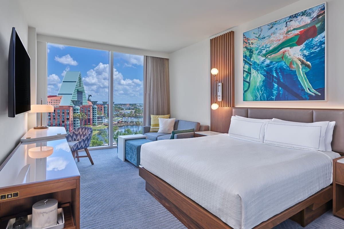 Een moderne hotelkamer met een groot bed, een bureau, een stoel, een televisie en een groot raam met uitzicht op de stad.
