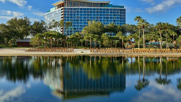 Un hôtel moderne doté d’une piscine aux eaux miroitantes, de palmiers et surplombant un ciel d’un bleu éclatant.