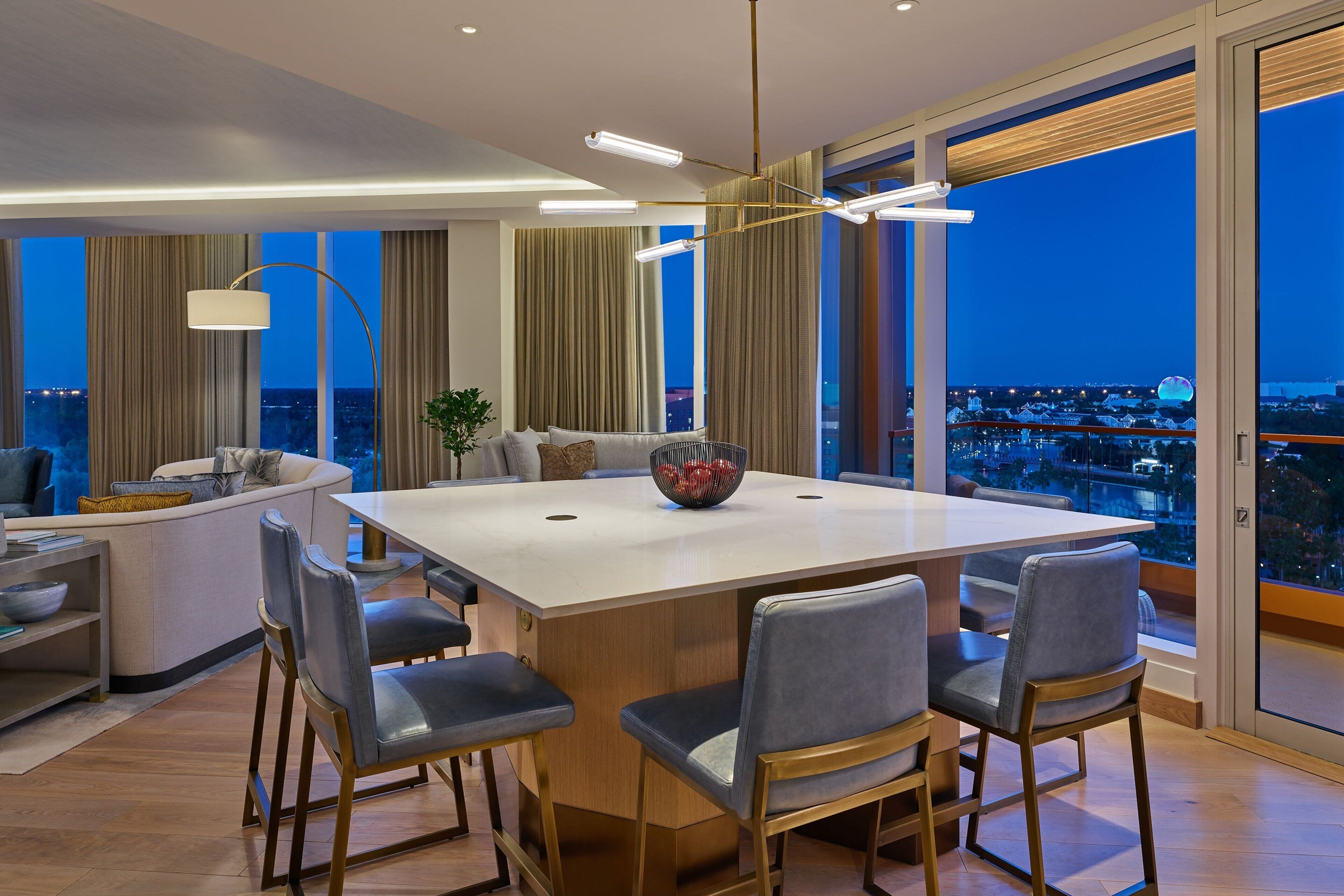 A modern dining area with a large table, six chairs, and a bowl of fruit.