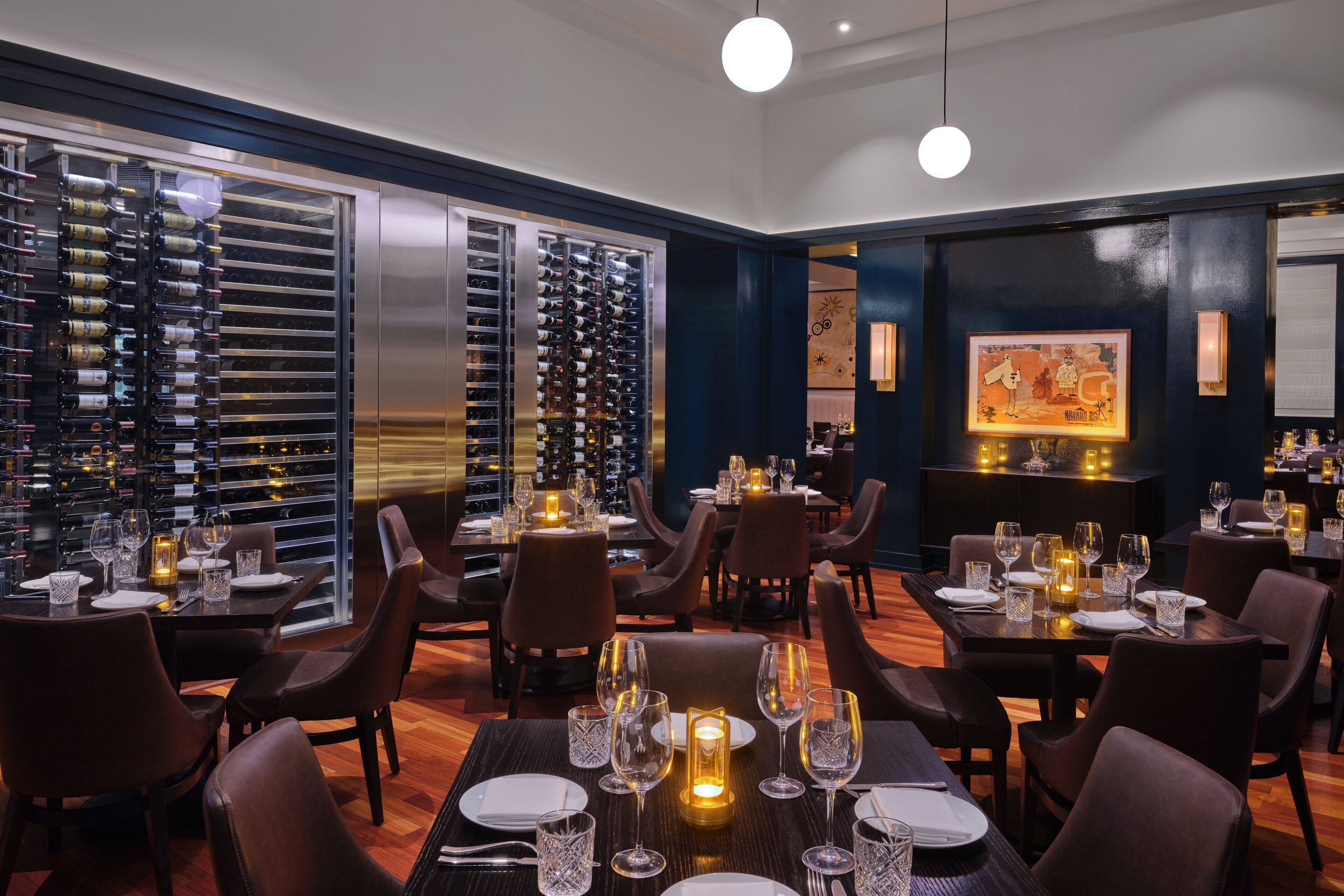 A restaurant with multiple dining tables set with candles, wine bottles, and glasses.