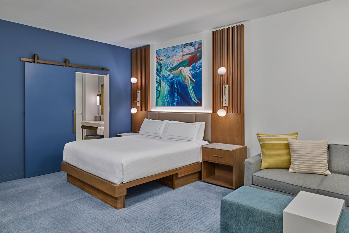 Een moderne slaapkamer met een bed, nachtkastjes, een bank en een groot schilderij aan de muur.
