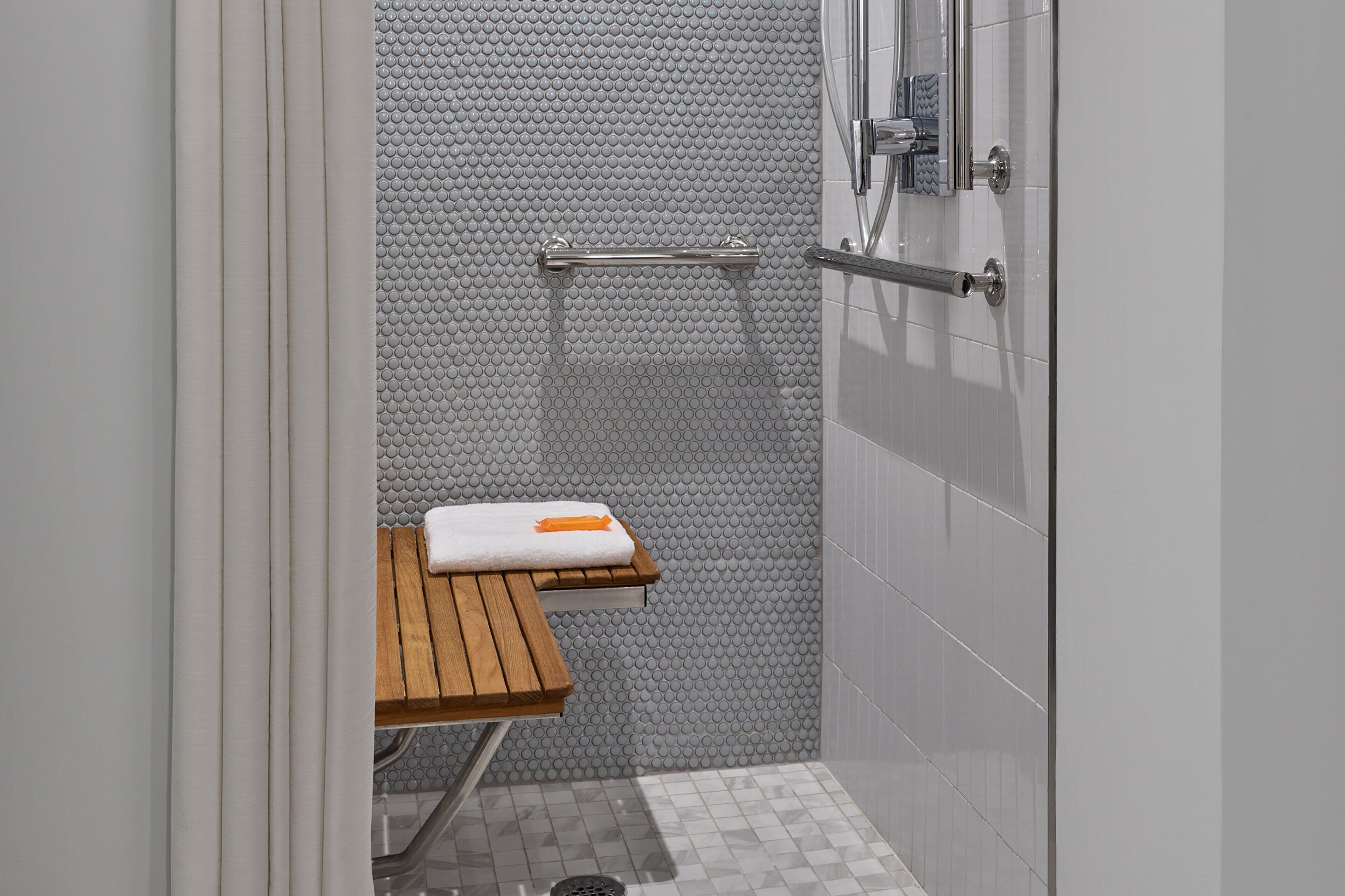 A shower area with a wooden bench, a towel, and a handrail.