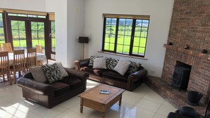A living room with leather sofas, a wooden coffee table, a fireplace, and large windows overlooking a green landscape. - Comeragh View Lodge (Kilmacthomas)