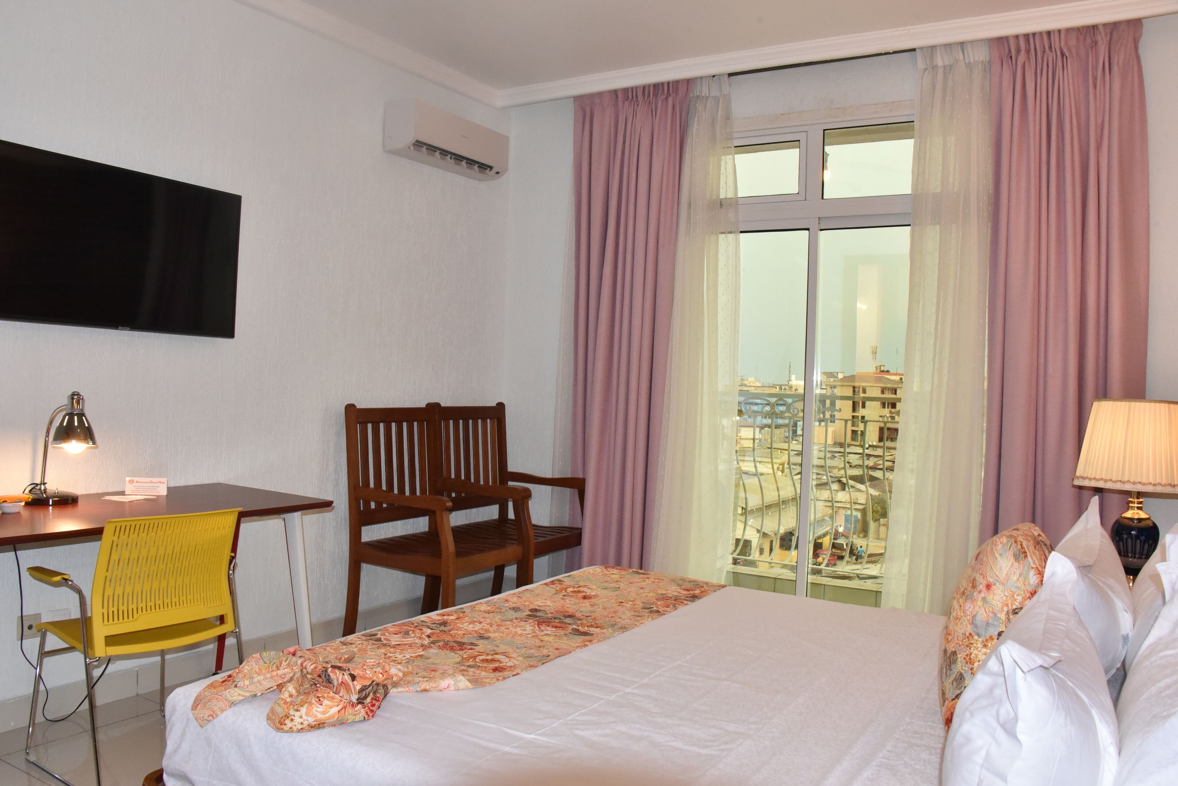 Hotelkamer met een bed, een bureau met stoel, een aan de muur bevestigde televisie en een raam met gordijnen.