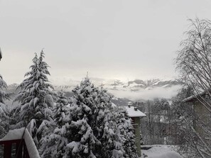 Un paisaje nevado con una cadena montañosa al fondo y un edificio con tejado cubierto de nieve.