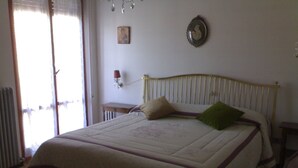 Een slaapkamer met een bed, een radiator, een raam met zonwering en een aan de muur hangend schilderij.