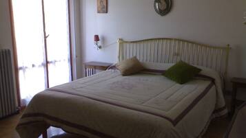 Een slaapkamer met een bed, een nachtkastje, een wandklok en een raam met gordijnen.