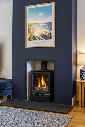 A modern living room with a fireplace, a framed picture of a coastal scene, and a blue sofa.