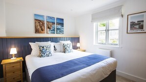 Une chambre à coucher avec un lit, une table de chevet, une fenêtre donnant sur la mer et un tableau encadré au mur.