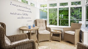 Une véranda meublée de mobilier en osier, une citation affichée sur le mur et une vue sur la verdure à l’extérieur.
