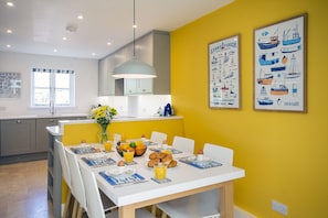 A bright yellow dining area with a white table set for breakfast, featuring croissants, orange juice, and a vase of flowers.