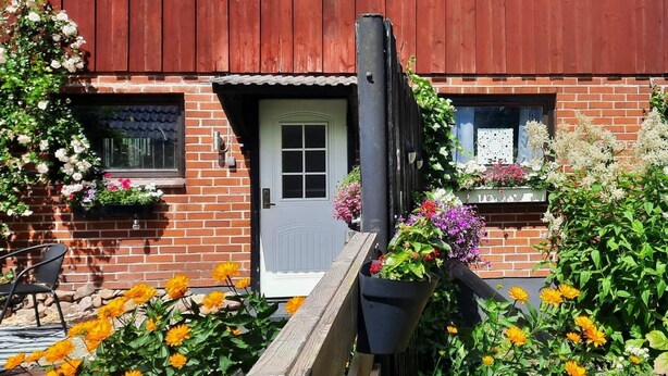 Un bâtiment en briques avec une porte blanche, un toit en bois rouge et des jardinières sur les rebords des fenêtres.