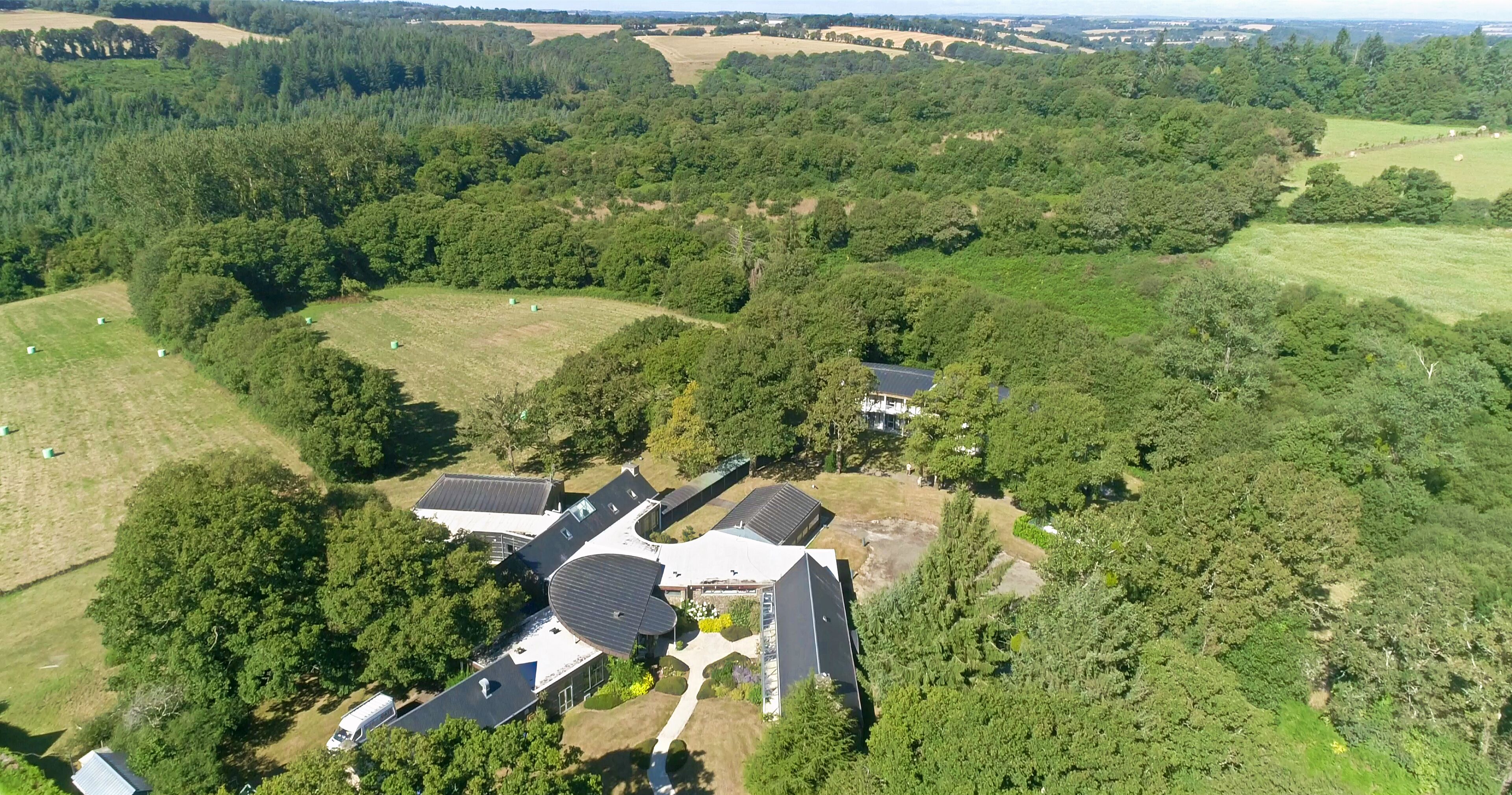 An aerial view of a residential area with multiple houses, surrounded by dense forests and open fields.