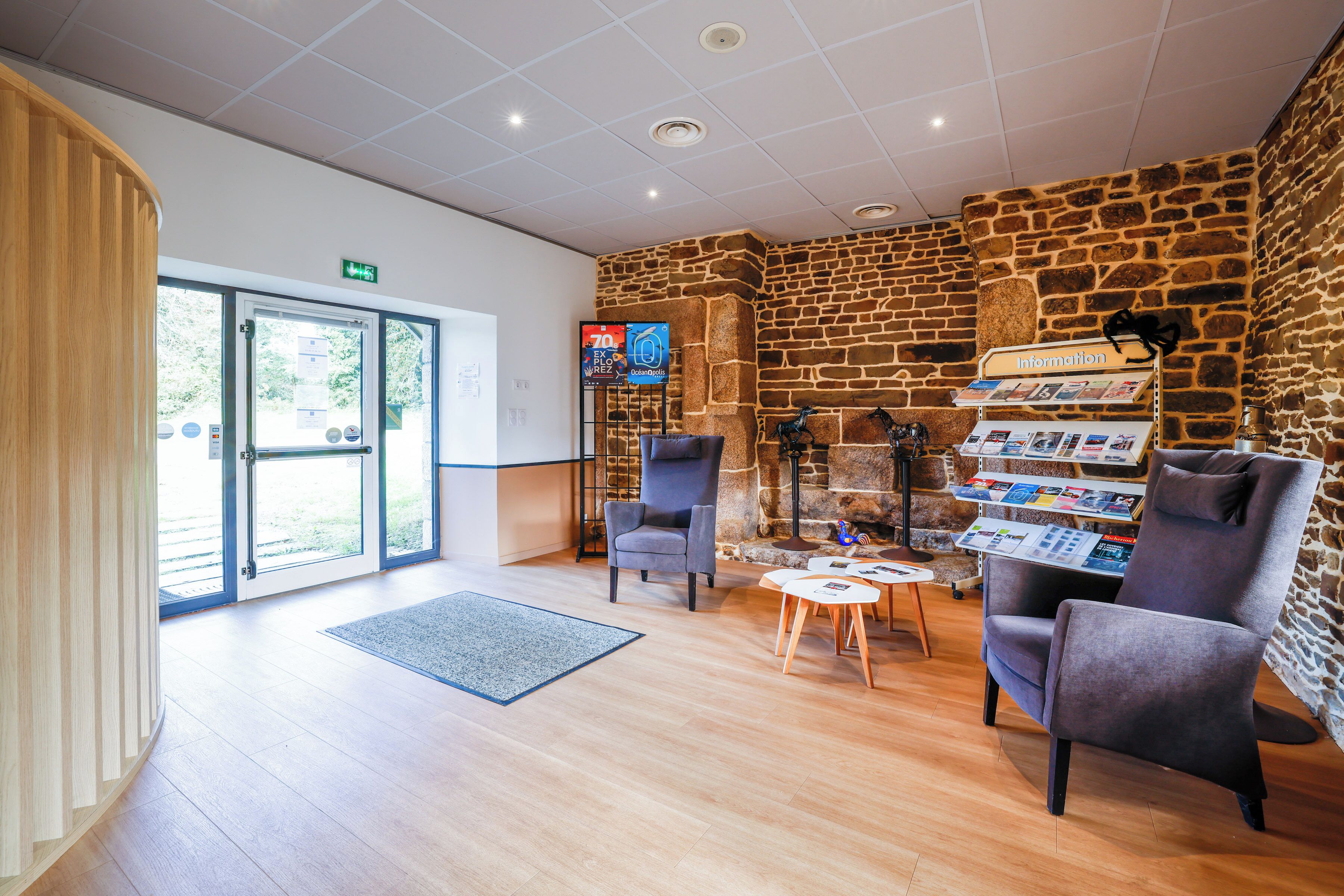 A lobby with a stone wall, two grey armchairs, a small table, and a reception desk with informational brochures.