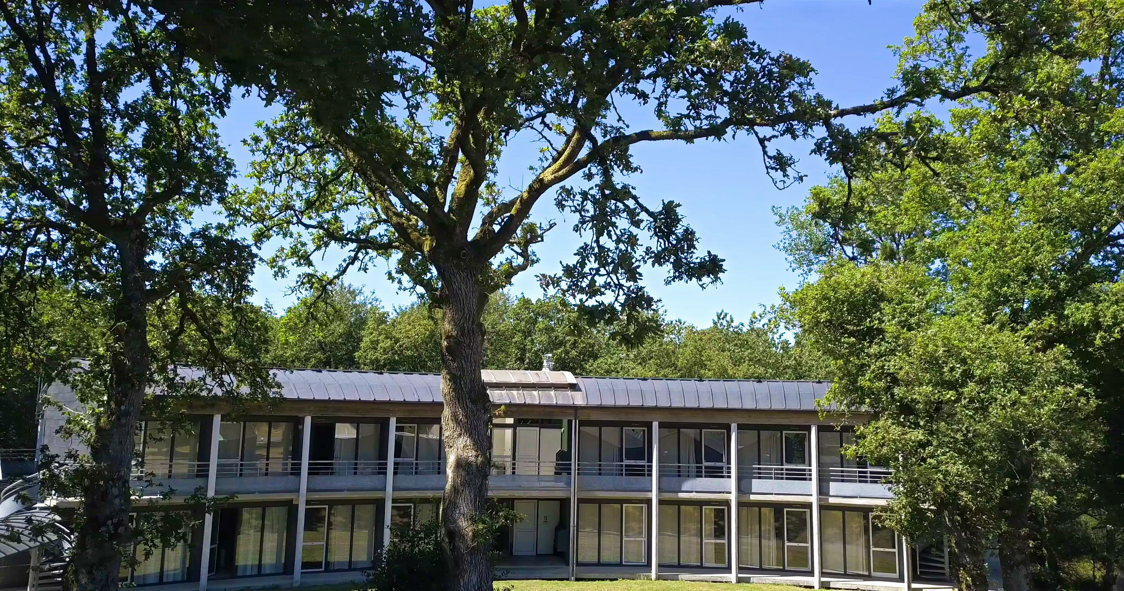 A modern building with a flat roof and large windows, surrounded by trees.