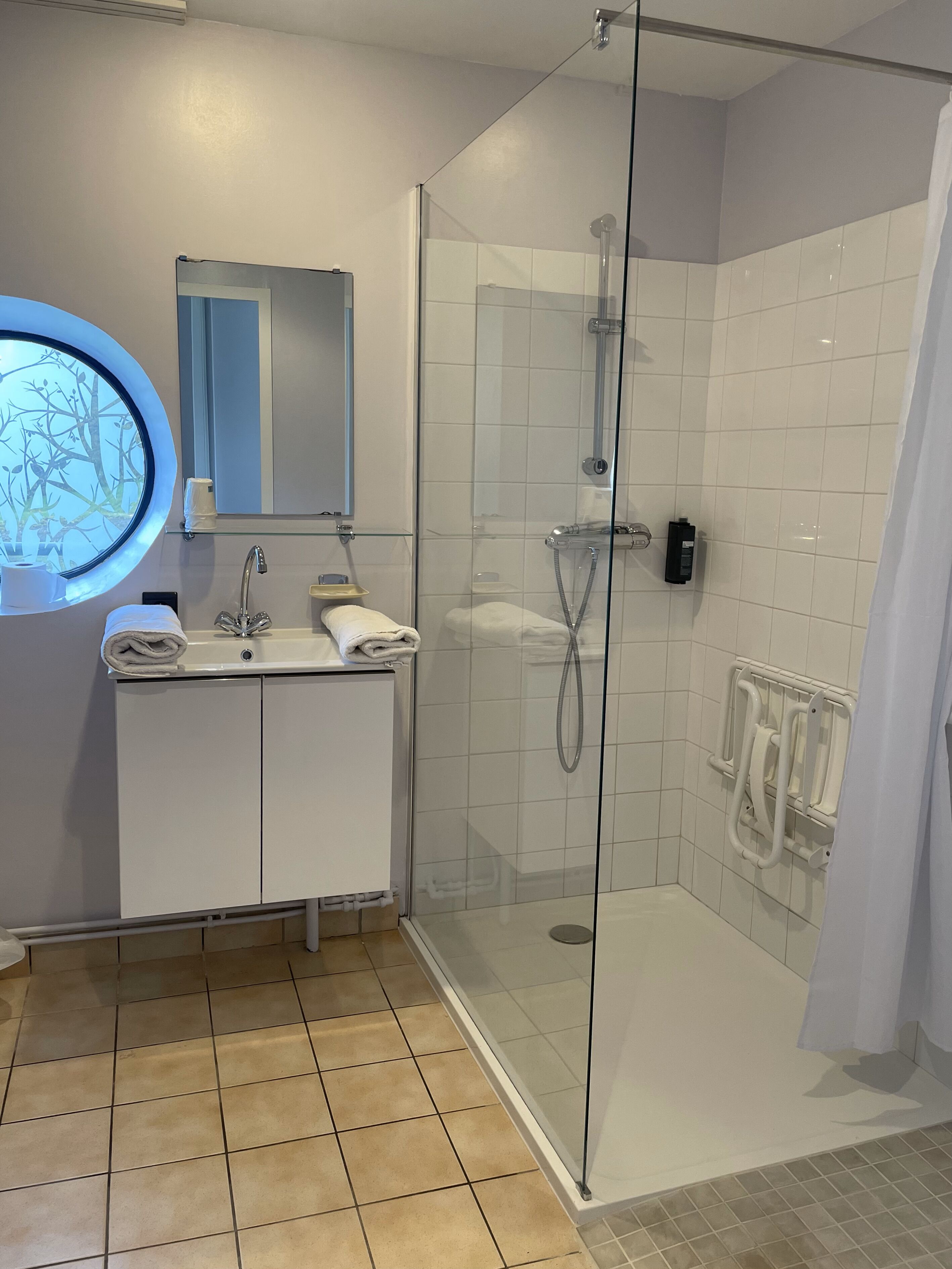 A modern bathroom with a glass-enclosed shower, a round mirror, and a white sink with a towel.
