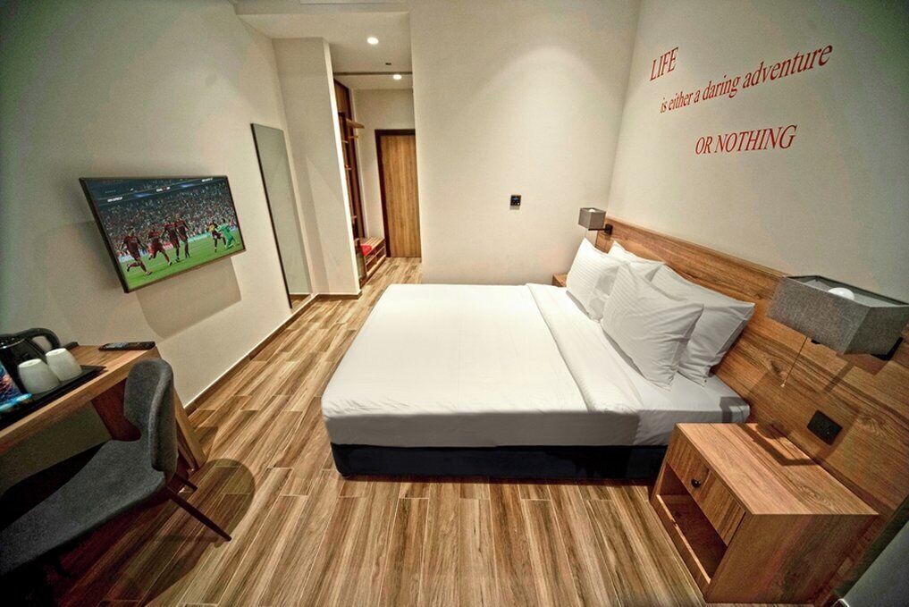 Habitación de hotel con cama, televisor montado en la pared, escritorio con silla y suelo de madera.