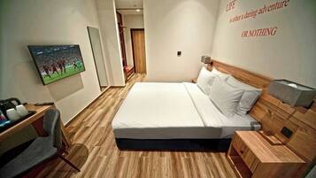 Habitación de hotel con cama, televisor montado en la pared, escritorio con silla y suelo de madera.