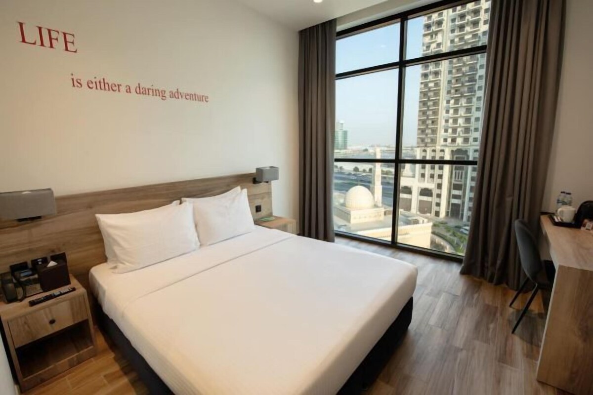 Quarto de hotel com uma cama grande, uma escrivaninha e vista para edifícios altos.